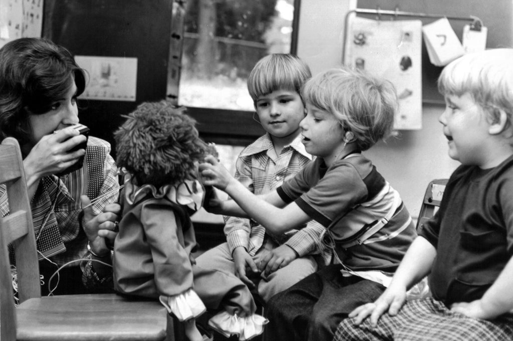 Anne Sullivan speaks through a speaker attached to a doll being played with by three young boys at Magnolia Speech School.