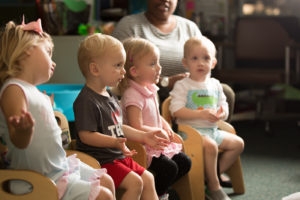 Very young children sit in a row and look off camera to teacher at Magnolia Speech School.
